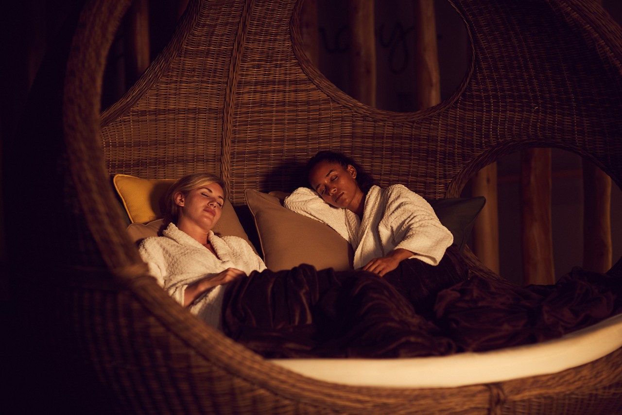 Two ladies relaxing under a blanket in a a large cocoon seat.